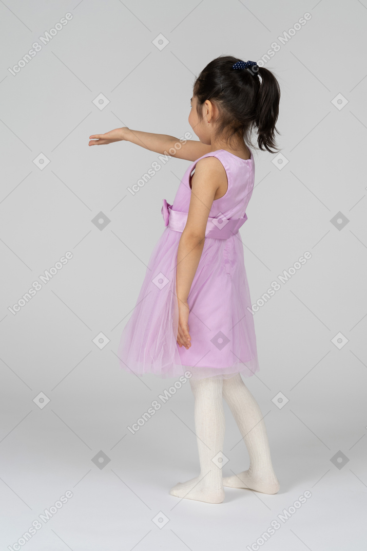 Three-quarter back view of a little girl in a tutu dress reaching out her right arm