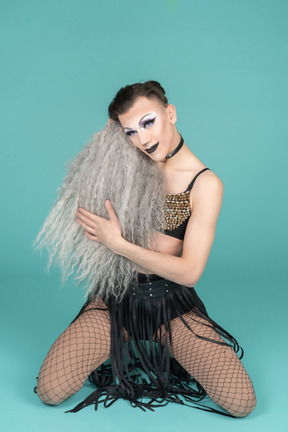 Drag queen standing on knees with gray wig in hands