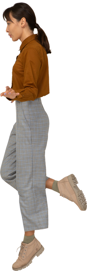Vista lateral traseira de uma jovem fêmea asiática pulando de calça e blusa estendendo as mãos