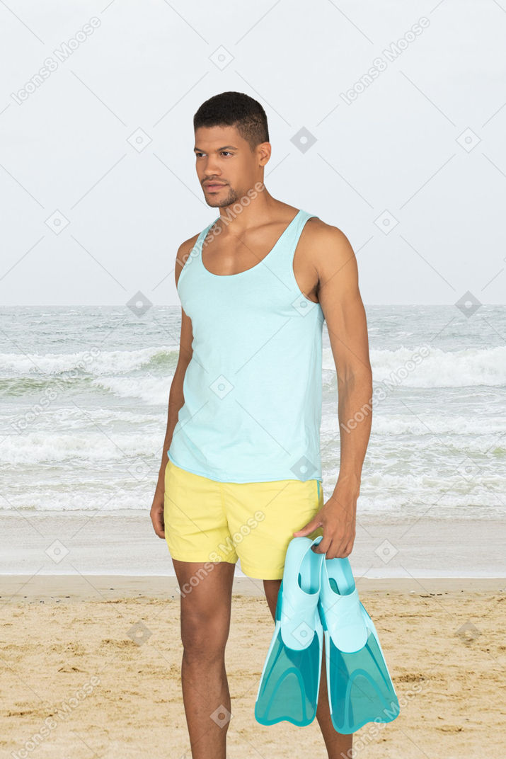 A man standing on a beach holding swimfins