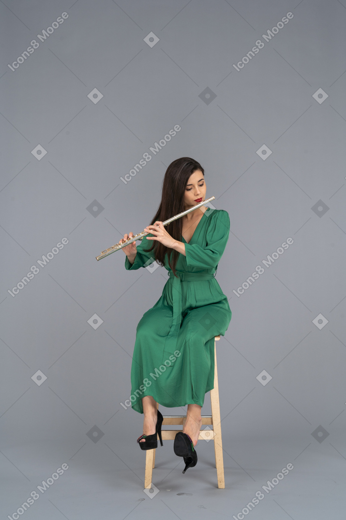 Vista frontal de uma jovem de vestido verde sentada em uma cadeira enquanto toca clarinete