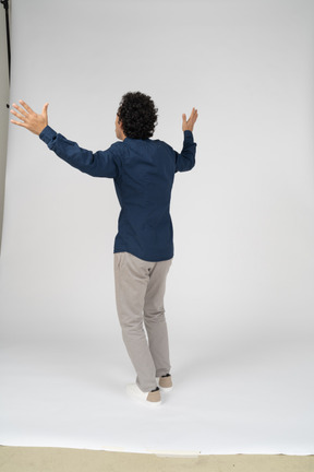 Вид сзади человека в повседневной одежде, стоящего с поднятыми руками