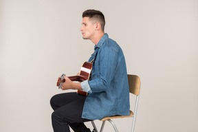 Young guy sitting on the table in profile and playing on guitar