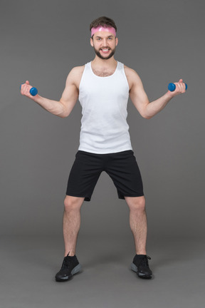 Expressive young man exercising with dumbbells