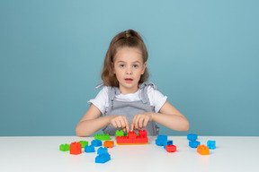 Bambina che gioca con i mattoncini lego e guarda l'obbiettivo