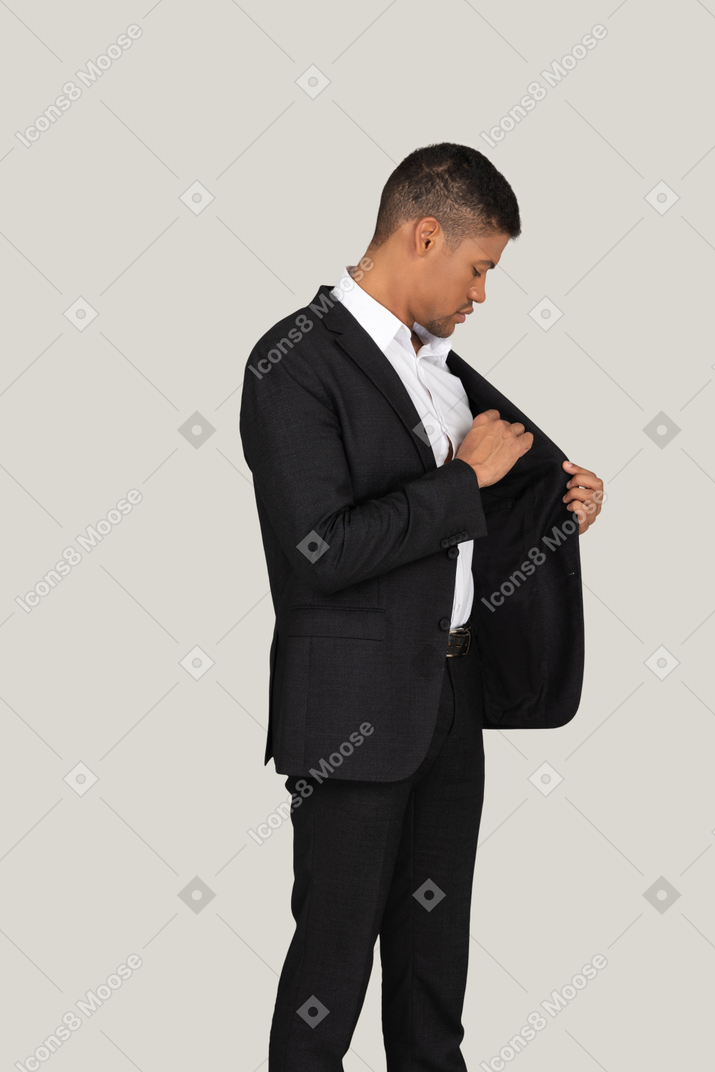 Vista lateral de um jovem de terno preto colocando algo no bolso