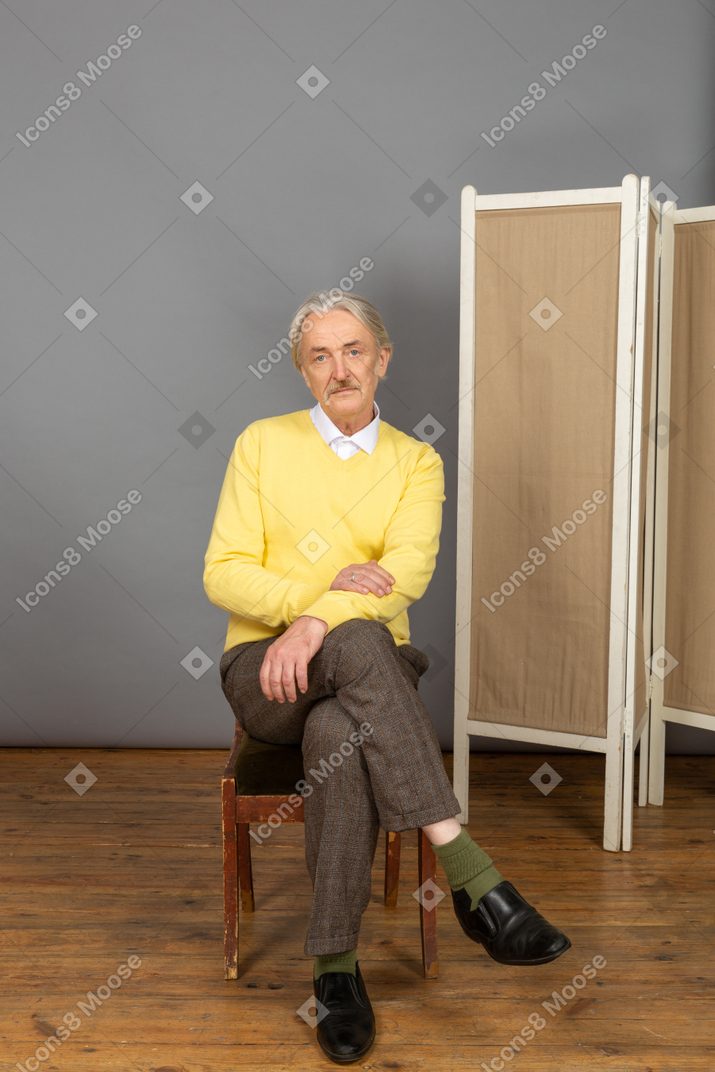 Мужчина сидит со скрещенными ногами и смотрит в камеру