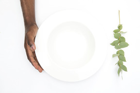 Черная мужская рука держит белую пустую тарелку