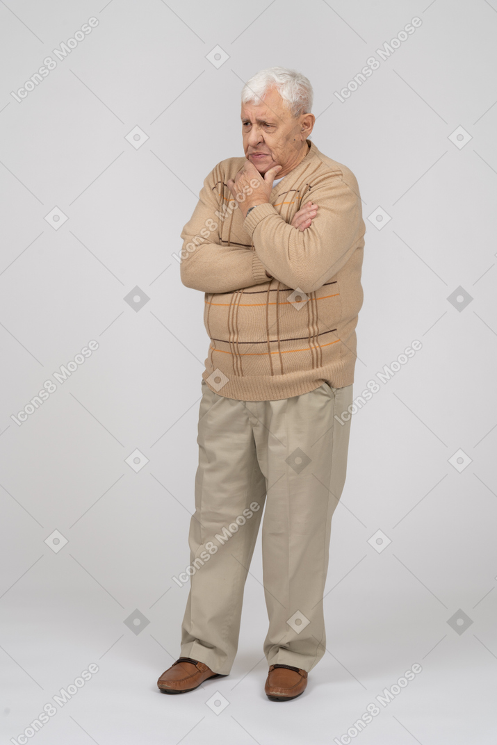 一位身穿休闲服、手放在下巴上站着的体贴老人的正面图