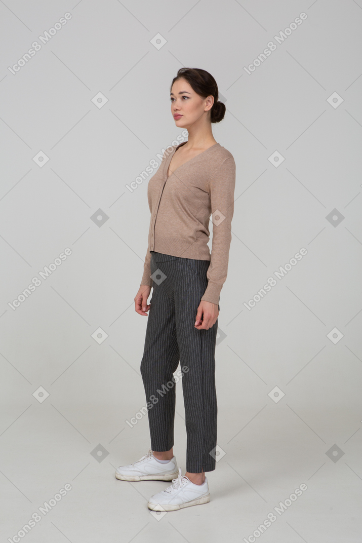 一位年轻女士在套头衫和裤子中站着的四分之三的视图