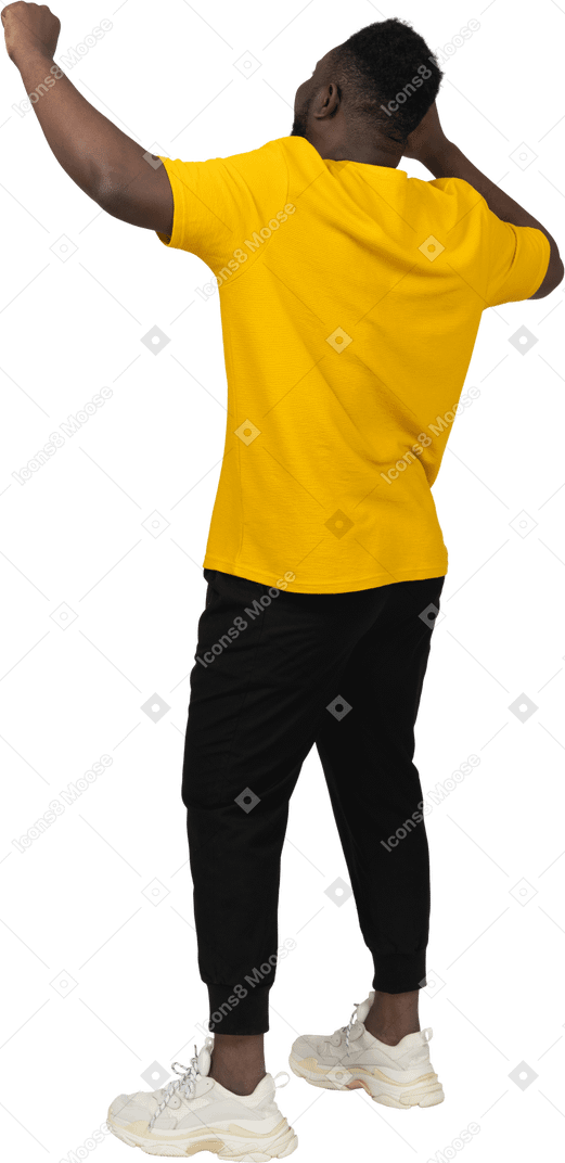 Vista posterior de tres cuartos de un feliz joven de piel oscura con camiseta amarilla levantando las manos
