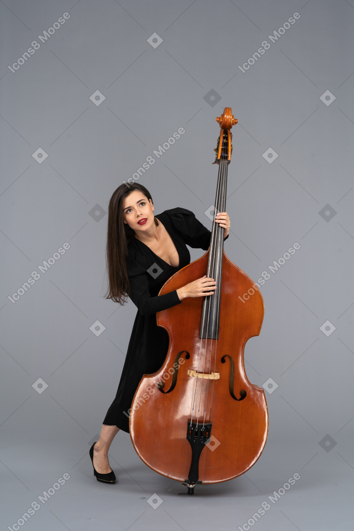 Front view of a young woman in black dress playing the double-bass wile looking up