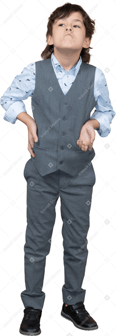 Vista frontal de um menino bonito de terno cinza posando com a mão no quadril e olhando para cima