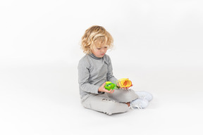 Ragazzo del bambino che si siede sul pavimento e che gioca con i giocattoli