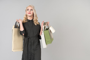 Uma jovem pessoa bonita de cabelos loiros em um vestido preto, segurando um monte de sacos de compras em ambas as mãos