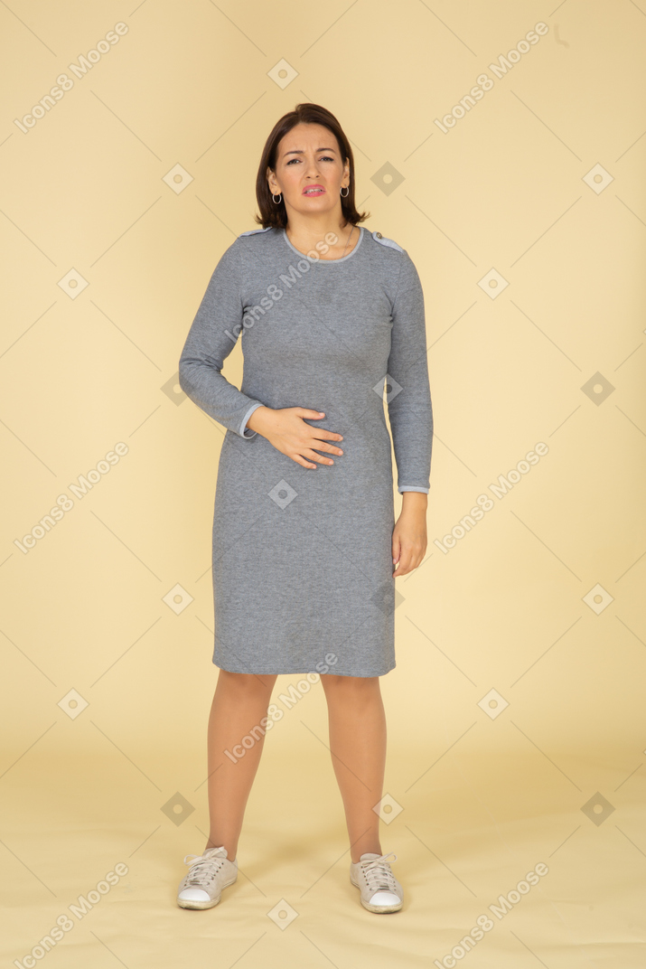 Vista frontal de uma mulher de vestido cinza sofrendo de dor de estômago