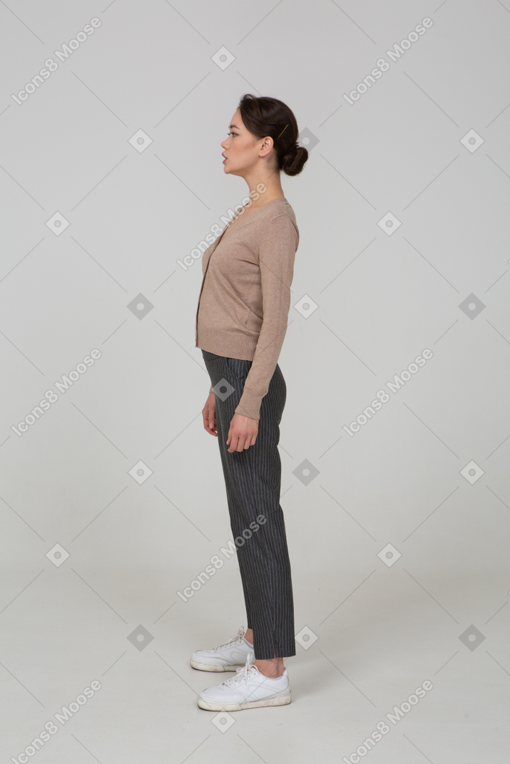 Вид сбоку молодой леди, стоящей в пуловере и штанах, смотрящей в сторону
