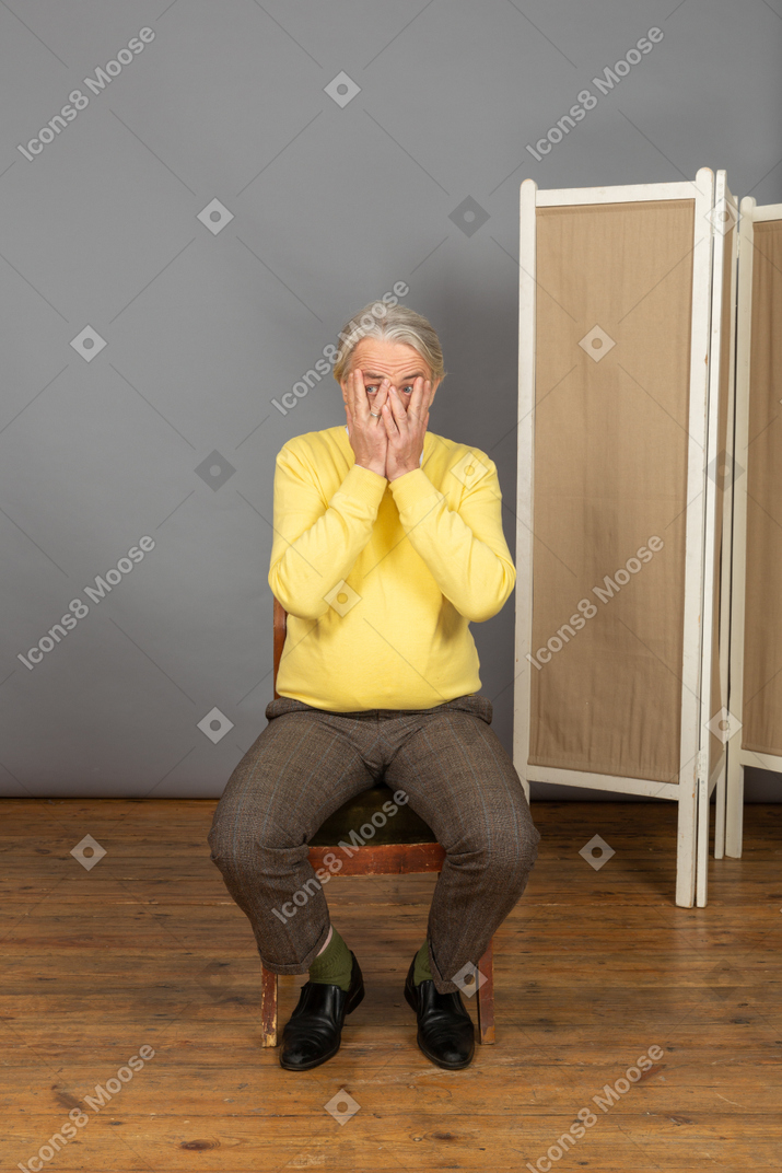 Homme d'âge moyen assis sur une chaise et couvrant son visage