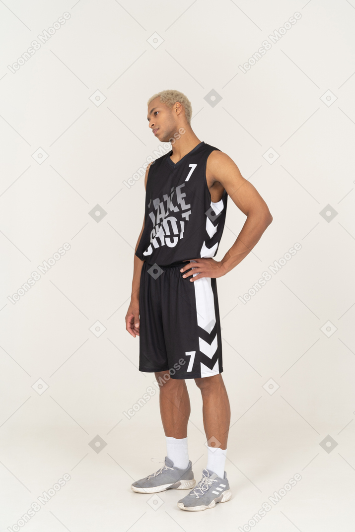 Dreiviertelansicht eines gelangweilten jungen männlichen basketballspielers, der die hand auf die hüfte legt