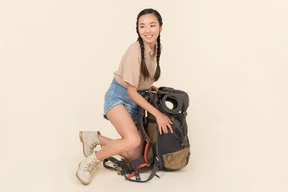Joven viajero femenino asiático sentado cerca de la enorme mochila turística