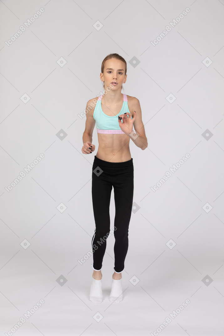 Vista frontal de uma adolescente em roupas esportivas, levantando as mãos na ponta dos pés