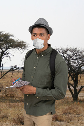 A man in a hat and green shirt holding pen and notepad