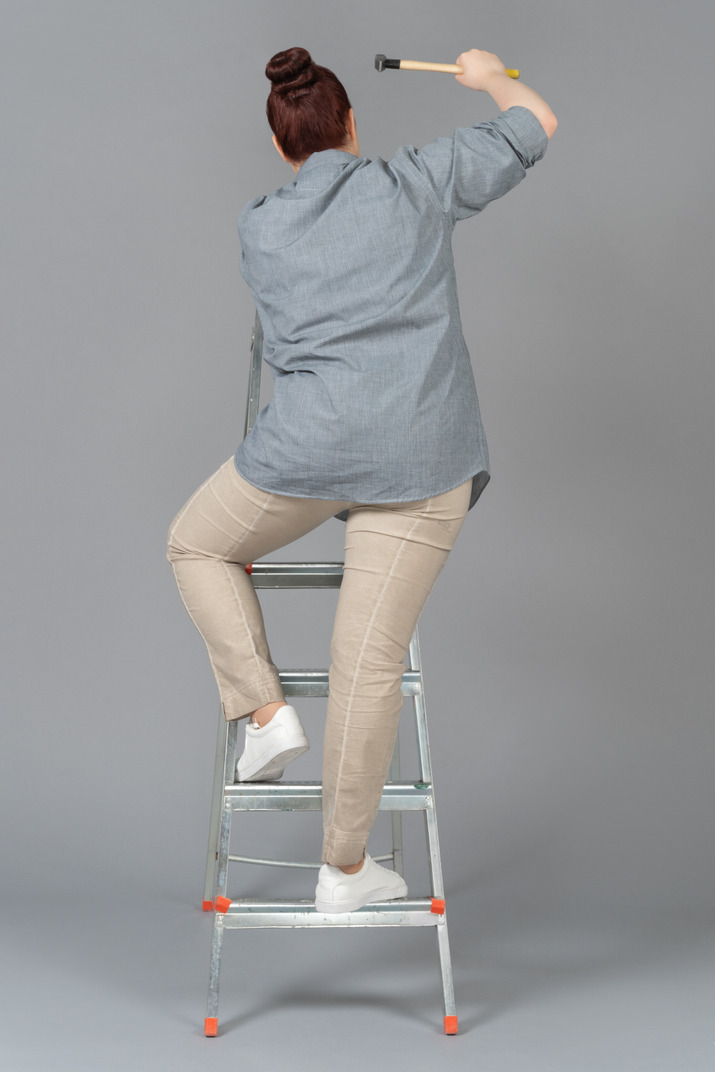 Young woman standing on stepladder backwards and hammering