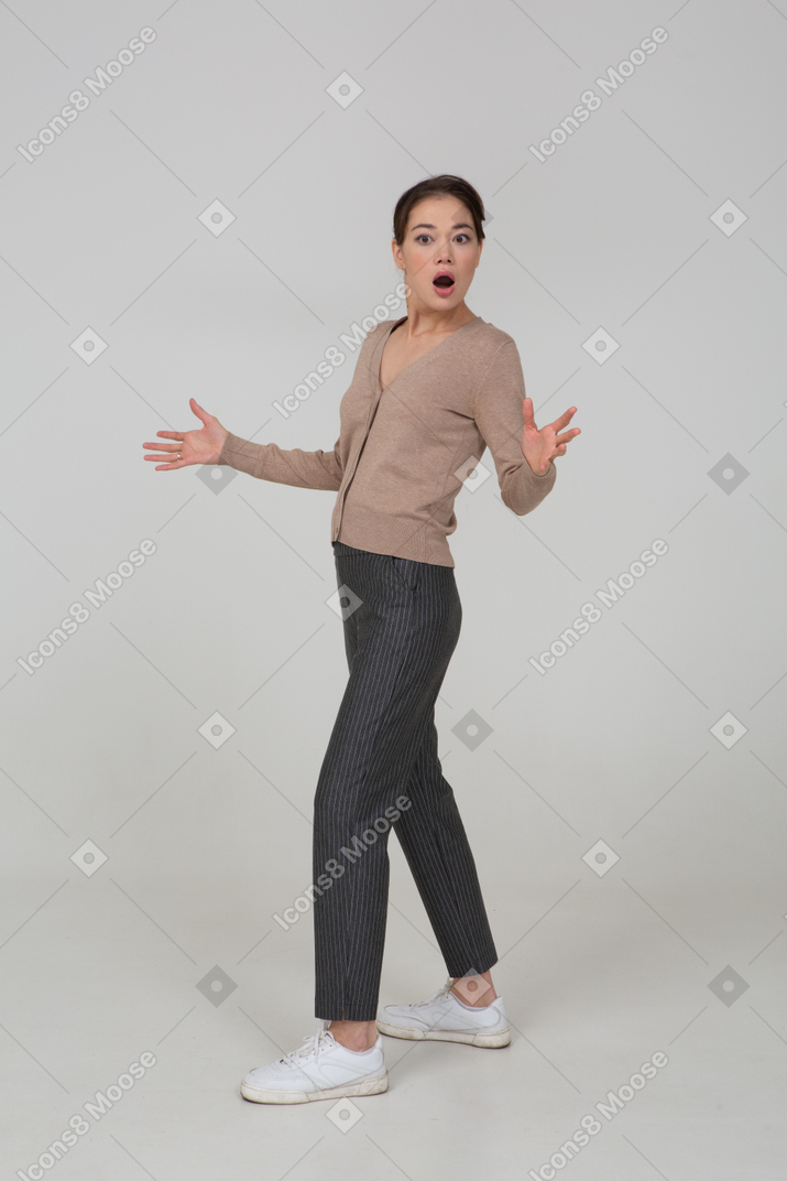 Вид в три четверти изумленной жестикулирующей молодой женщины в бежевом пуловере