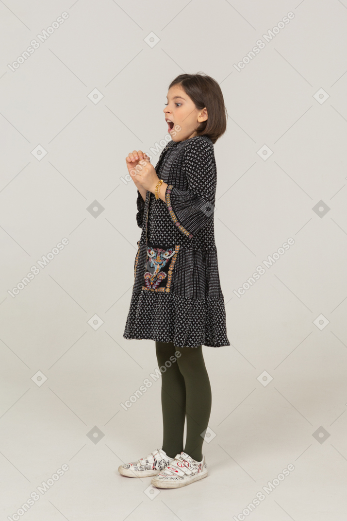 Vista laterale di una bambina eccitata in abito stringendo i pugni