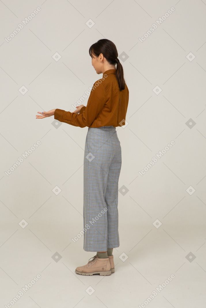 Three-quarter back view of a questioning young asian female in breeches and blouse raising hands