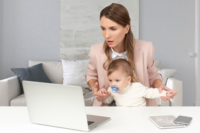 A woman with a baby in front of a laptop