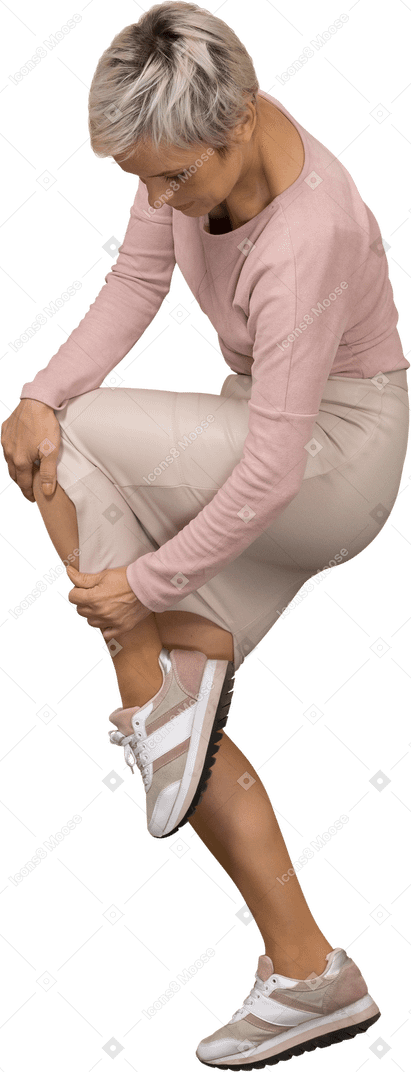 Vista lateral de una mujer en ropa casual de pie con la pierna levantada y mirando la falda