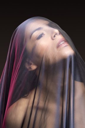 Close-up of sensual naked young woman in dark veil looking up
