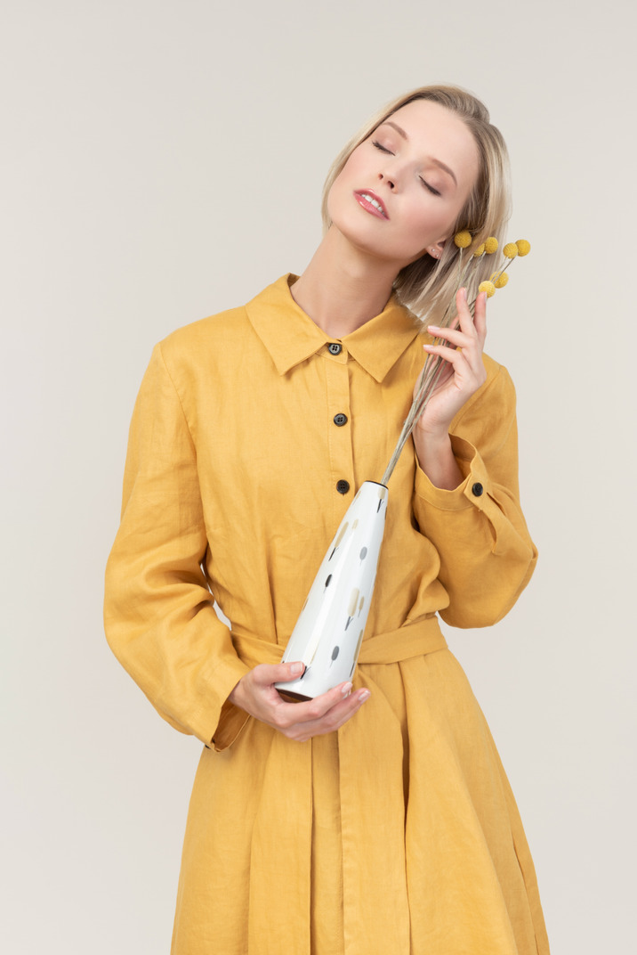 Young woman in yellow dress holding vase with eyes closed