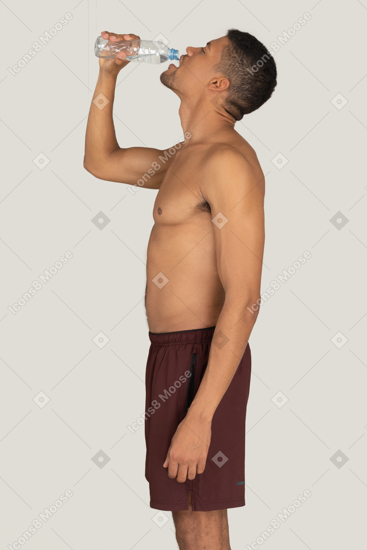 Standing in profile young man in sport shorts drinking water