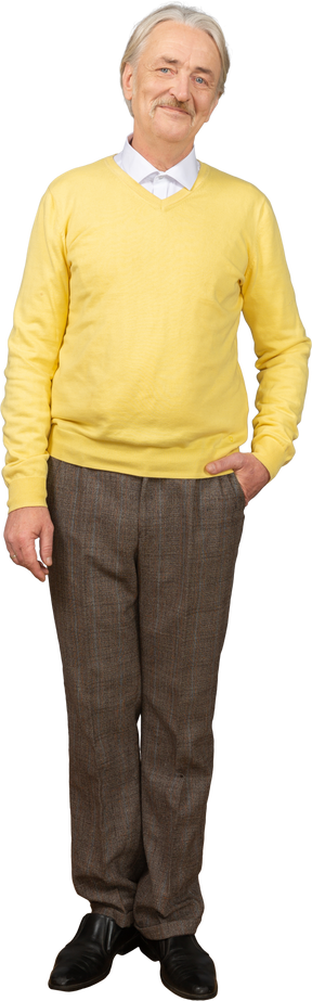 Vista frontal de un anciano complacido en un jersey amarillo poniendo la mano en el bolsillo y mirando a la cámara