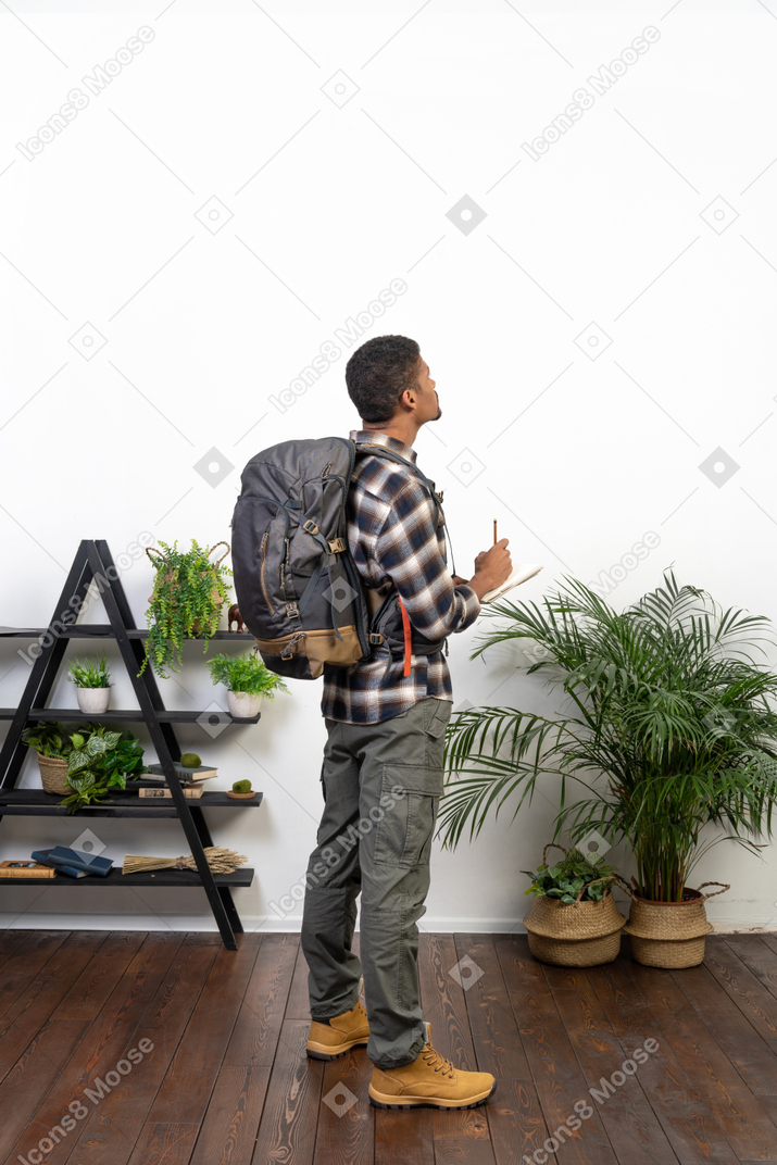 Vista traseira de três quartos de um turista com uma mochila e um bloco de notas
