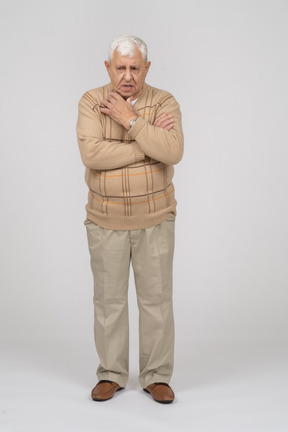 Front view of an old man in casual clothes standing with hand on shoulder