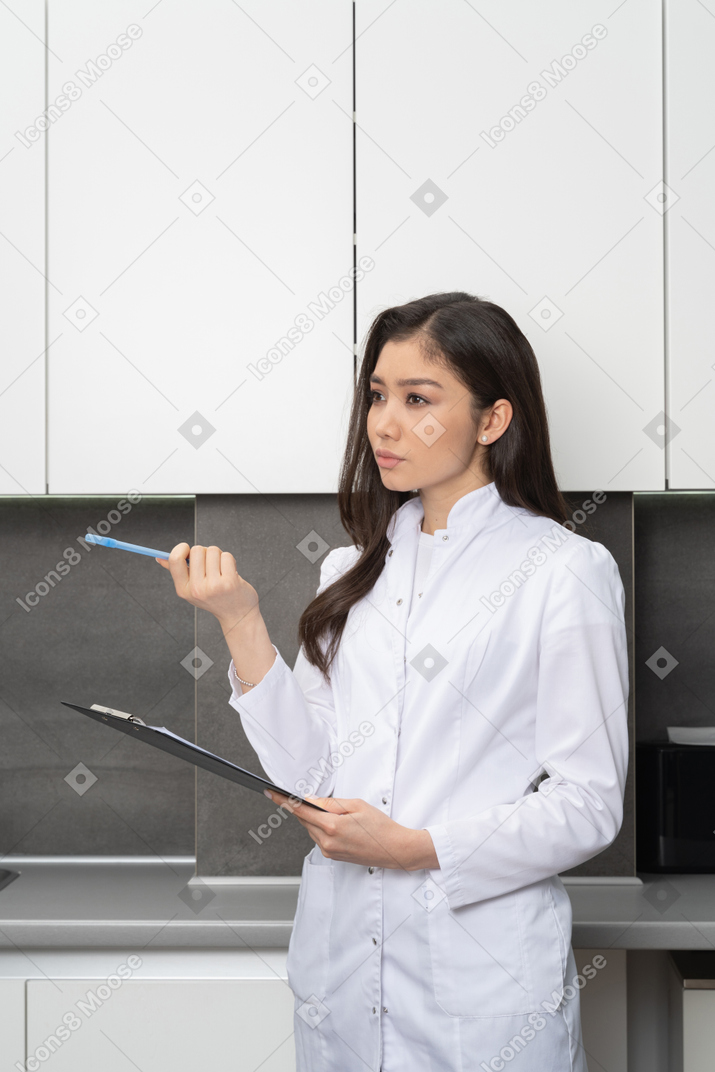 Three-quarter view of a female doctor pointing pen and holding her tablet