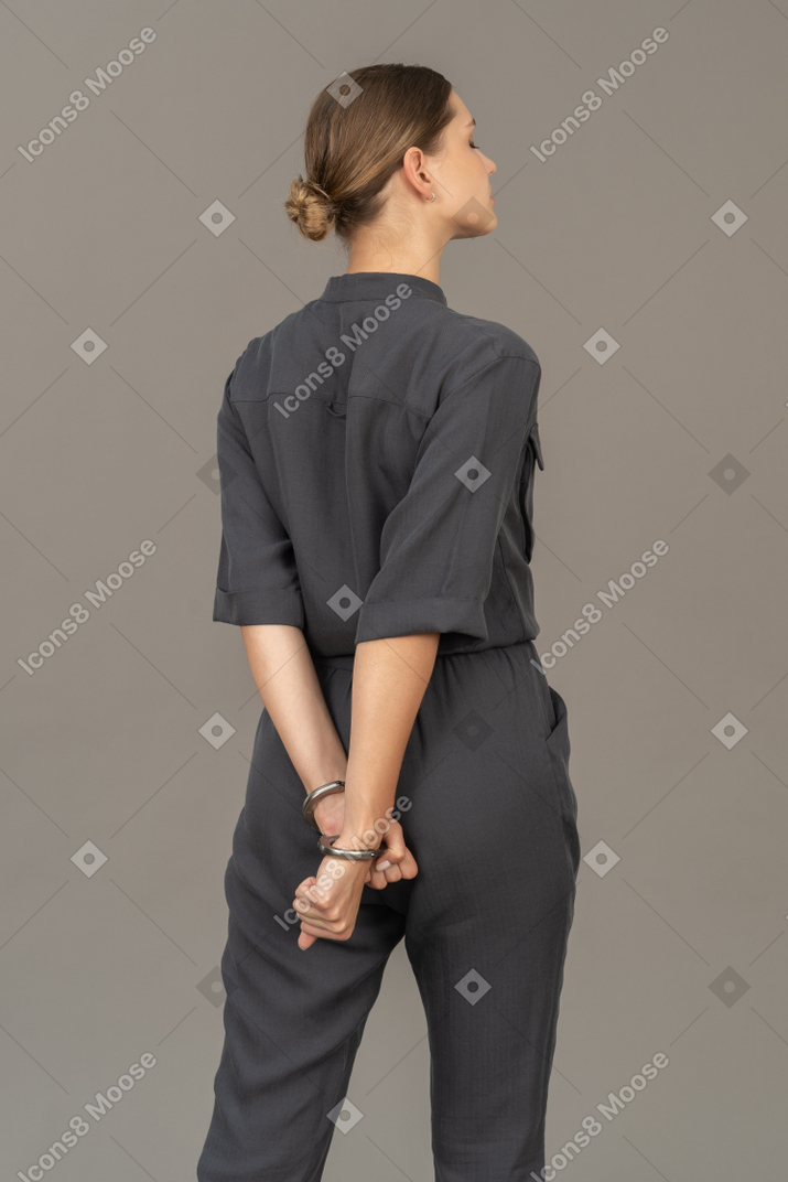 Vue de trois quarts arrière d'une jeune femme en combinaison portant des menottes