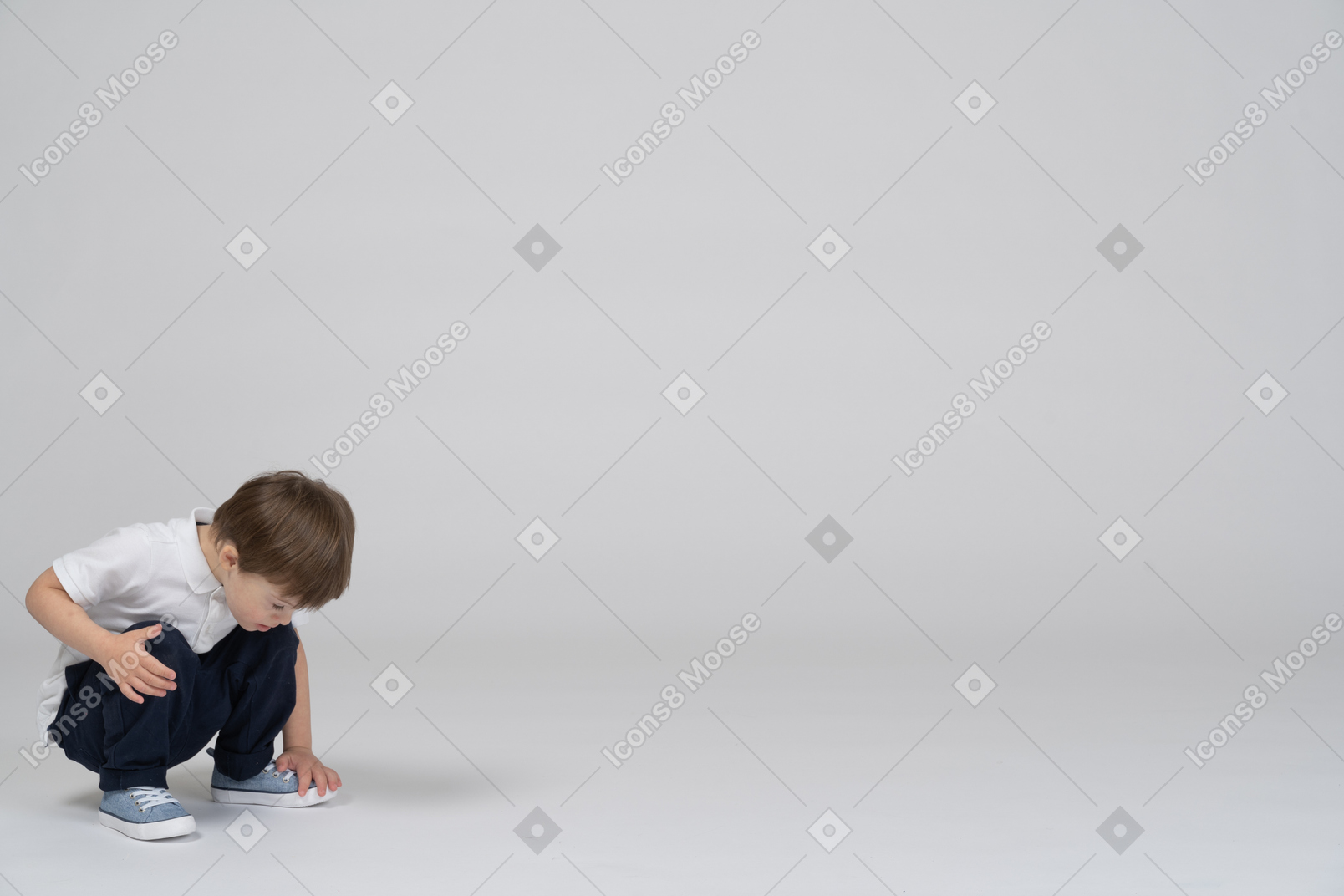 Приседающий маленький мальчик в повседневной одежде