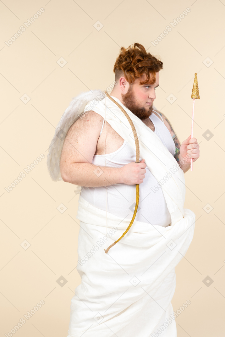 Mad looking young man dressed as a cupid holding bow and arrow
