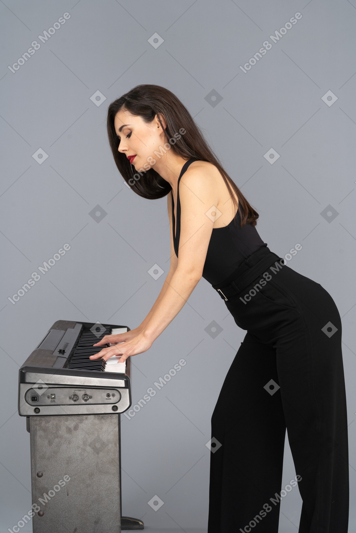 Side view of a young lady in black suit playing the piano