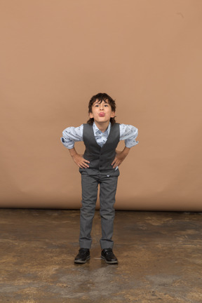 Front view of a boy in suit standing with hands on hips and bending down