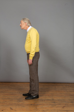 Side view of an old surprised man in yellow pullover leaning forward and looking aside