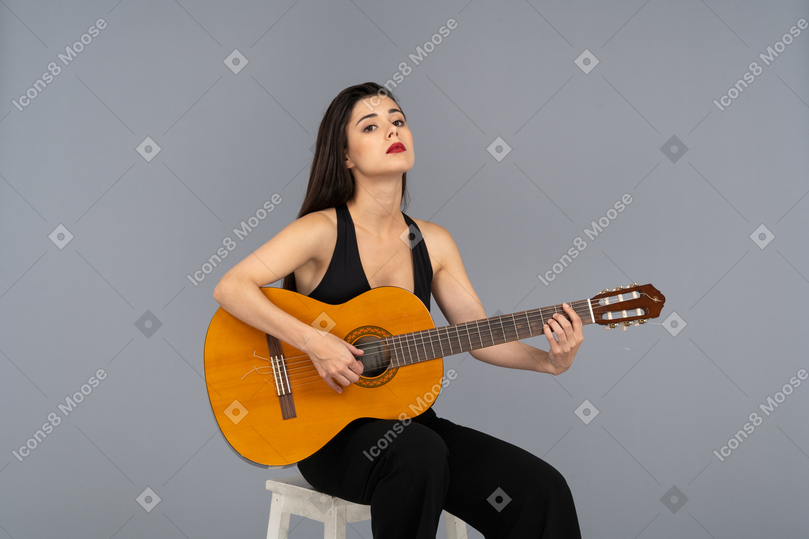 Vista frontal de una joven sentada en traje negro sosteniendo la guitarra y levantando la cabeza