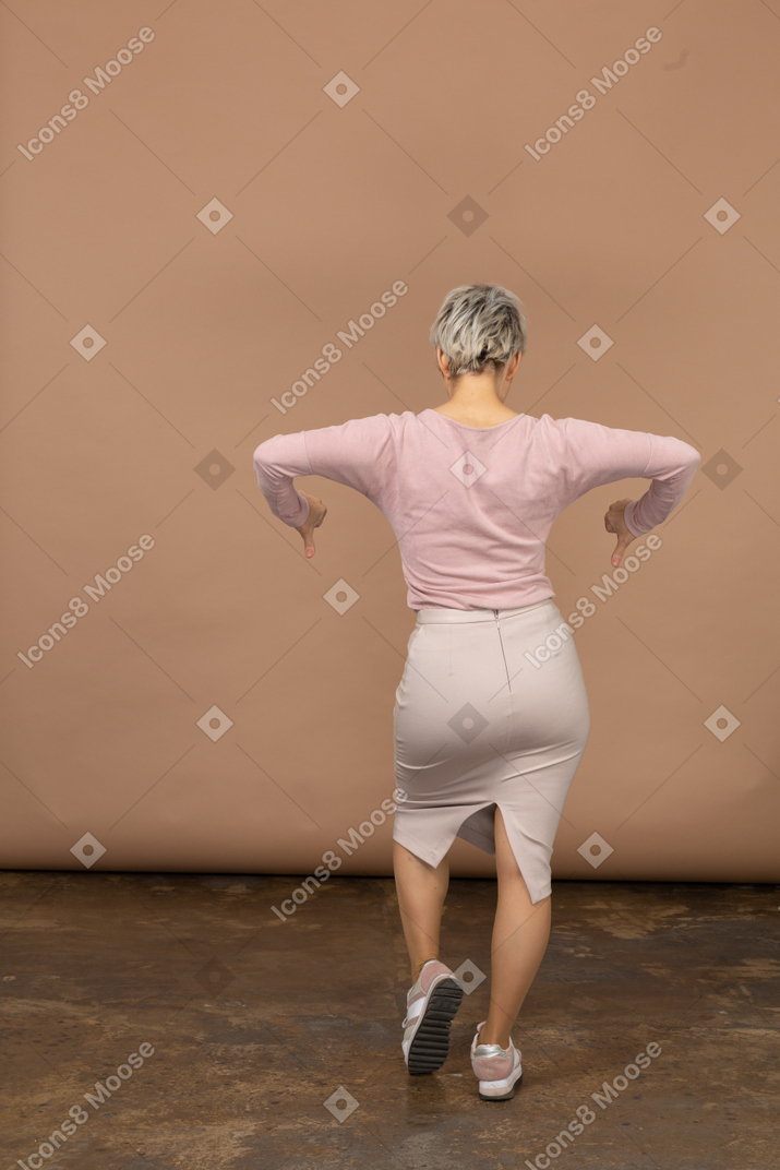 Вид сзади женщины в повседневной одежде показывает палец вниз