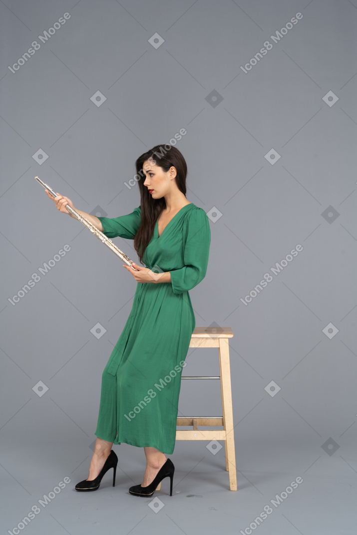 椅子に座ってクラリネットを保持している緑のドレスを着た若い女性の側面図