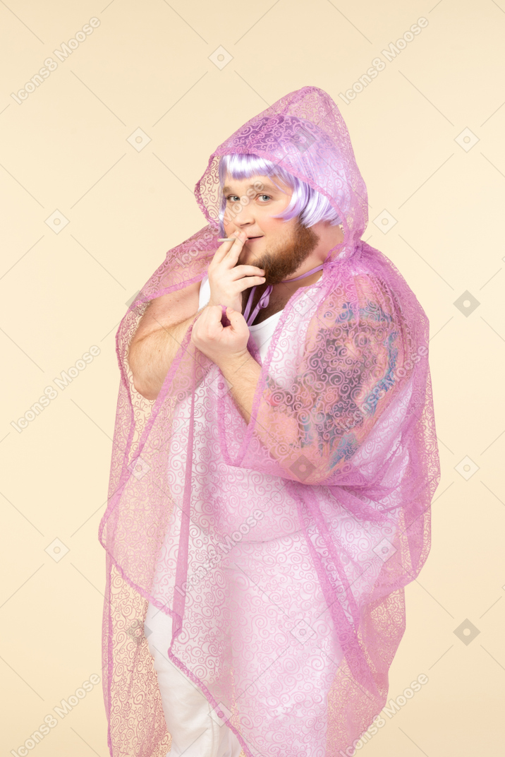 Jeune homme grassouillet en cape de fée violette fumant une cigarette