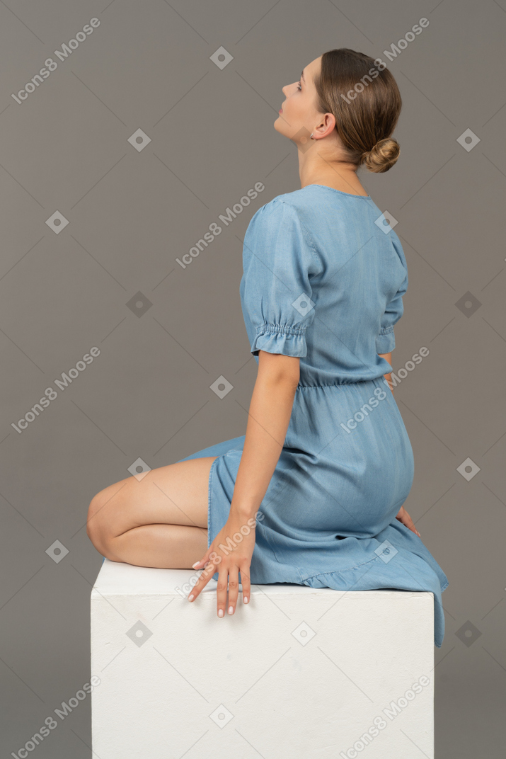 Rückansicht einer jungen frau im blauen kleid, die auf einem würfel sitzt
